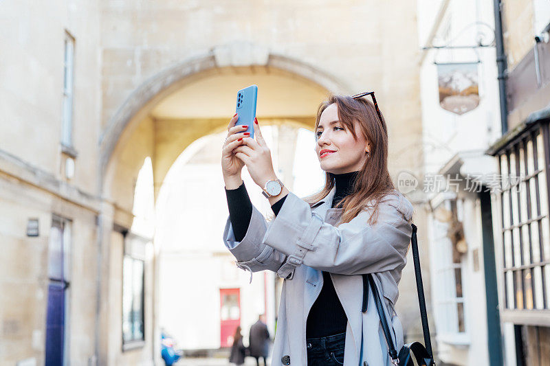 年轻的女游客参观风景如画的城市街道目的地，在假期和旅行期间用智能手机拍照，在古老的欧洲城市，户外散步。游览市区。