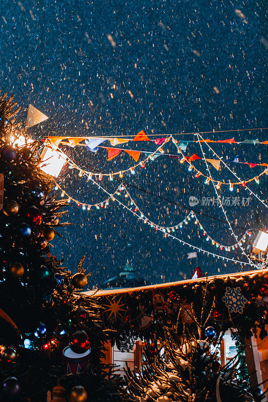 圣诞树和漫天飞舞的雪花在夜晚的灯光下，营造出喜庆神奇的新年气氛。
