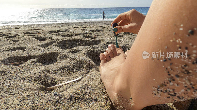 年轻女子在沙滩上涂指甲