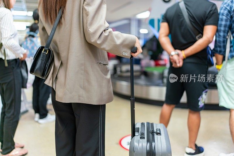 年轻的亚洲女商人在机场行李提取处等候行李