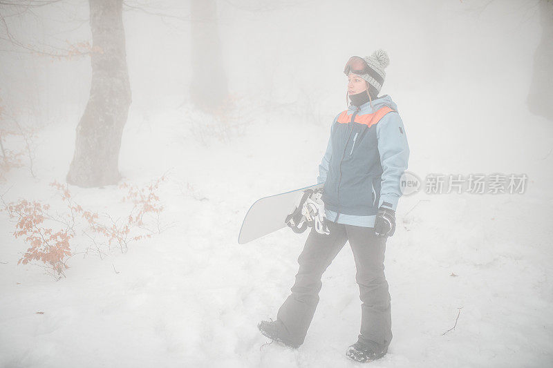 一个女滑雪板运动员准备在山上滑雪的全长视图，在冬天