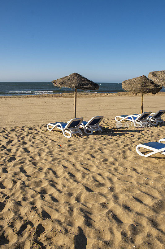 美丽的夏日西班牙海岸景观，几个日光浴躺椅，日光浴躺椅和遮阳伞。金色细沙，地平线海景，蓝天，平静放松。鼓舞人心的度假景观。