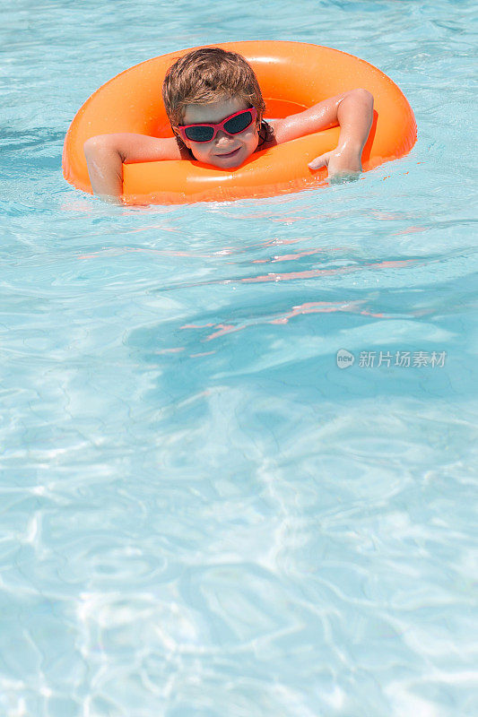 带着充气圈微笑的男孩在游泳池里游泳。