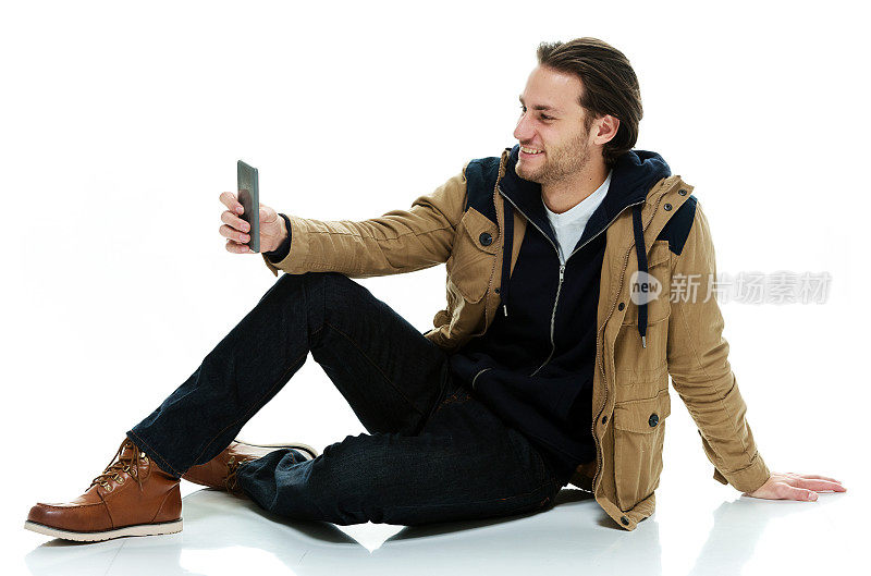 微笑的休闲男子坐在地板上使用手机