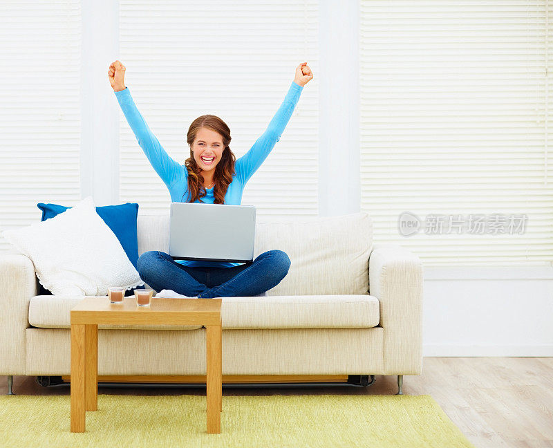 快乐的年轻女性胜利举起双手，在家里用笔记本电脑