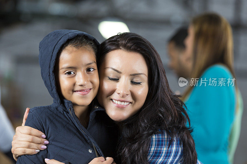 西班牙裔母亲拥抱年轻的女儿在社区大衣驱动器