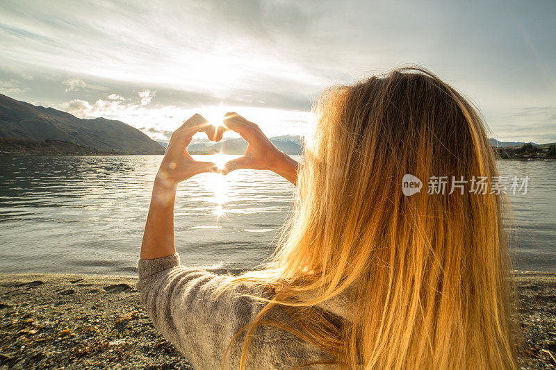 女性在湖山景观上做心形指架