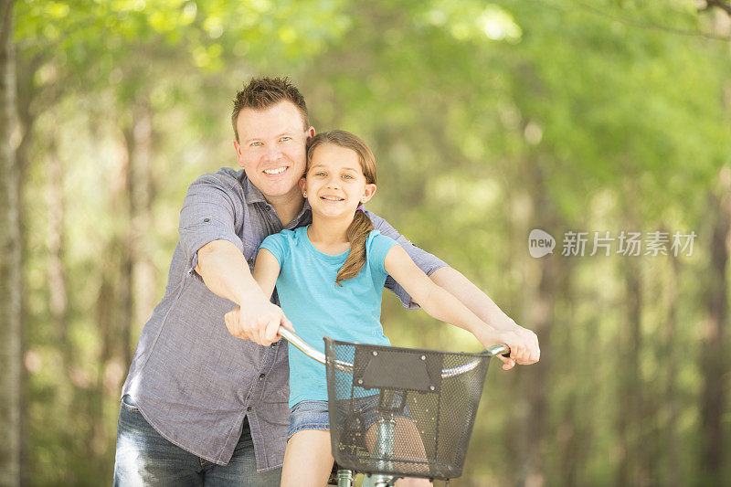 和爸爸一起骑自行车。小女孩，爸爸在外面。院子里。夏天。