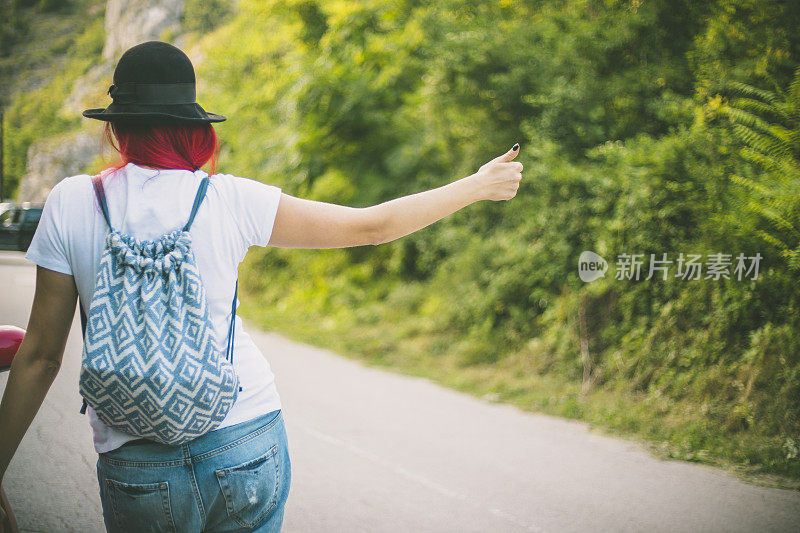 带着帽子和背包的女孩在路上搭便车