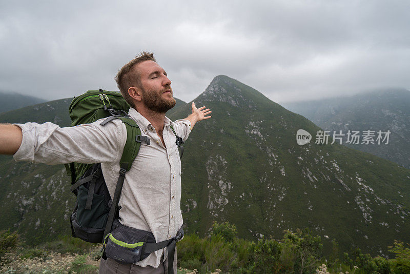 一位年轻的男徒步旅行者在山顶张开双臂