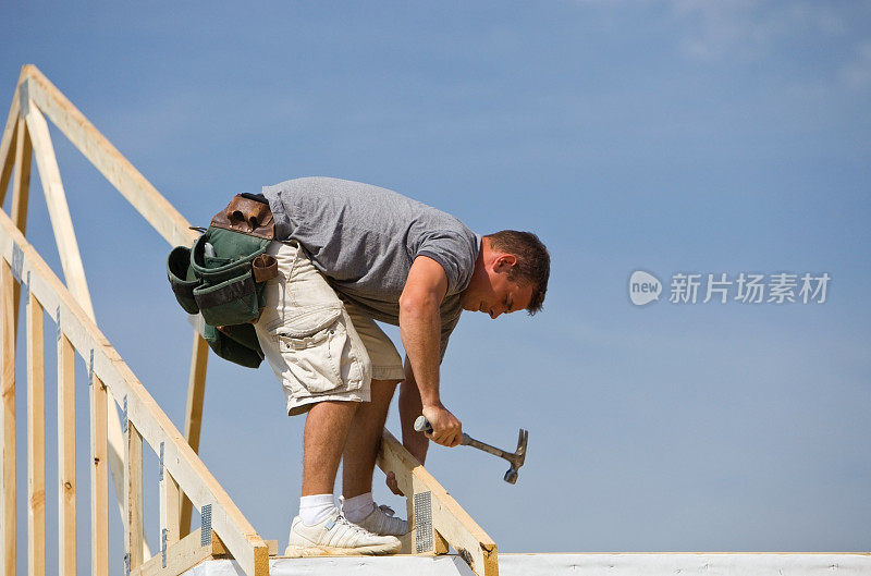 建筑者在蓝天下敲打屋架上的钉子