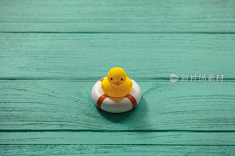 一只橡皮鸭放在一张旧的绿松石木桌上，上面有一个安全的充气环。