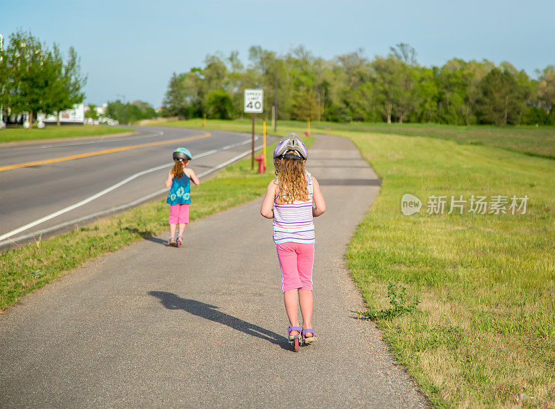 后视图两个女孩骑摩托车在铺平的道路上