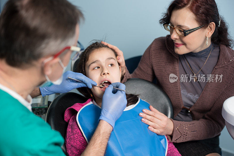 小女孩和妈妈第一次看牙医。资深儿科牙医在牙科诊所为病人做第一次检查。牙科、医学和保健理念。牙科设备