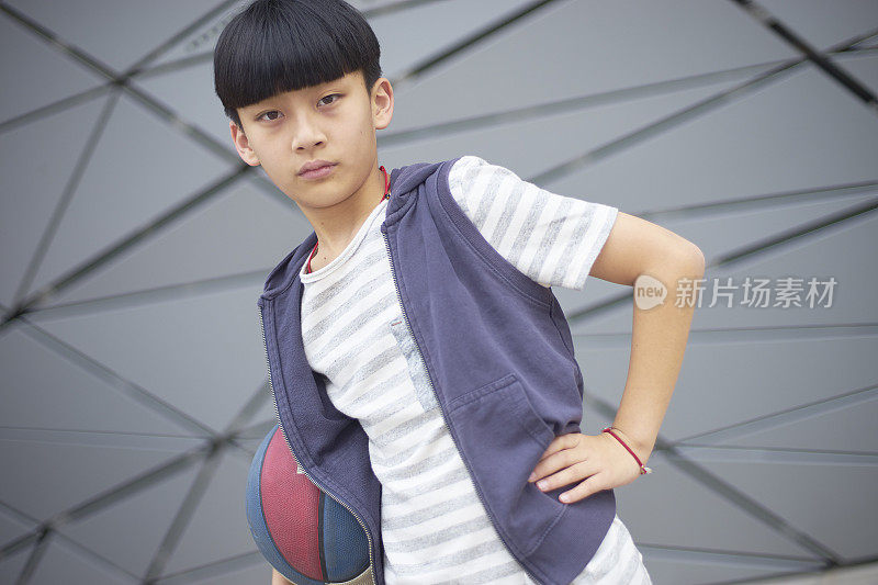 酷酷的亚洲孩子在户外拿着篮球的肖像
