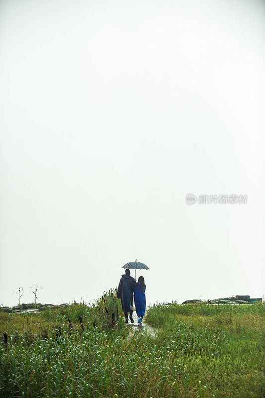 背对远处的夫妻在雨中走在一起的雨衣和雨伞