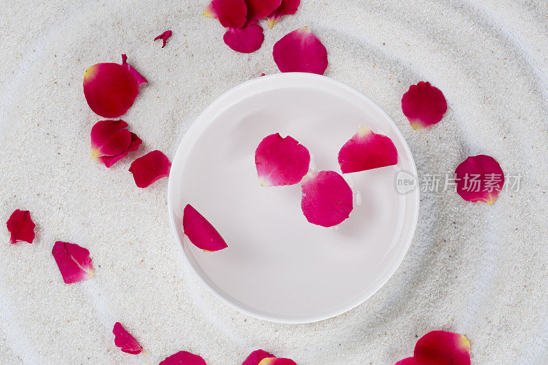 白色的碗里放着玫瑰花瓣，还有白色的沙子。水疗中心。