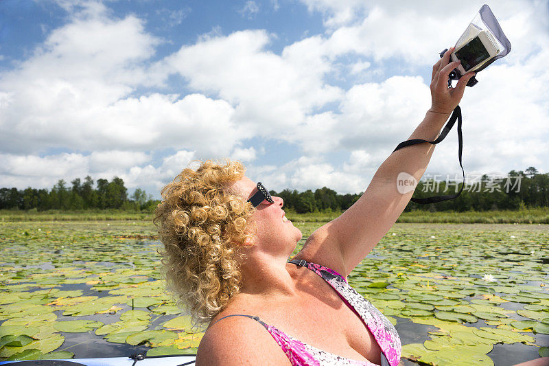 美国明尼苏达州哈肯萨克十英里湖，一名40多岁的成年白人女性用智能手机上的塑料防水保护套安全自拍