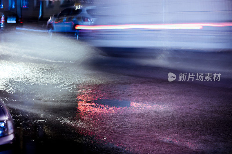 大雨时，红色的前灯反射在被淹没的道路上。模糊的汽车在运动。