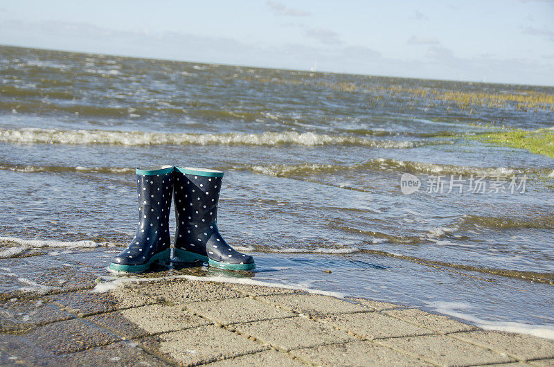 蓝色的孩子们的橡胶靴子在海上孤零零地站立着，海水很快就会淹没它们