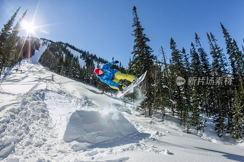 在森林和山脉的背景下，滑雪自由人从雪坡上跳下来