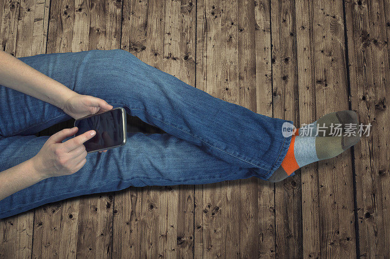 穿着牛仔裤坐在家里地板上玩手机的女孩。