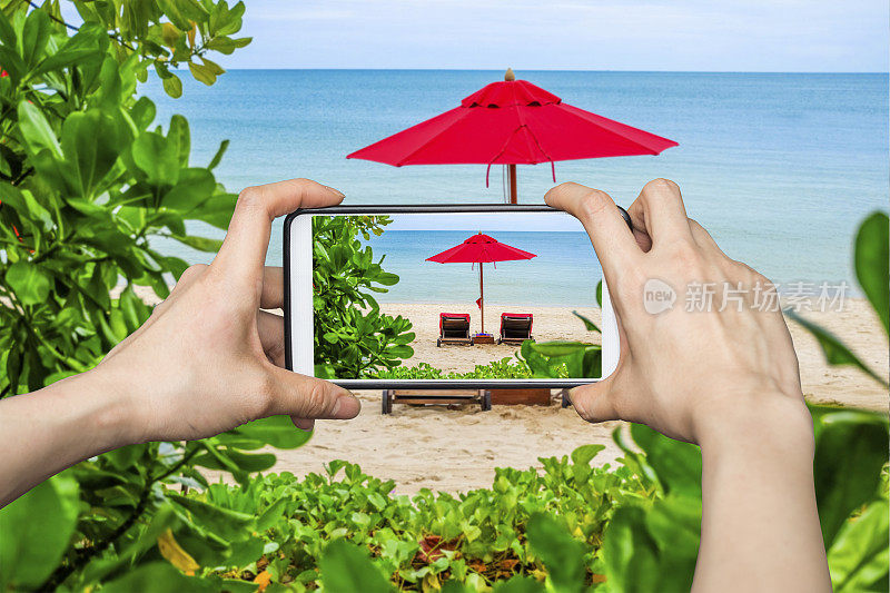 一名正在用手机拍照的女子在海滩上展示红伞