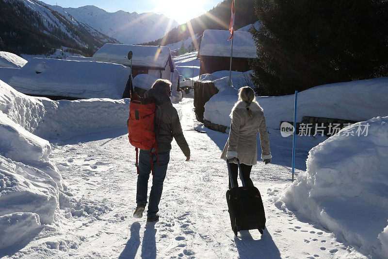男人和女人拉着手提箱穿过白雪覆盖的村庄
