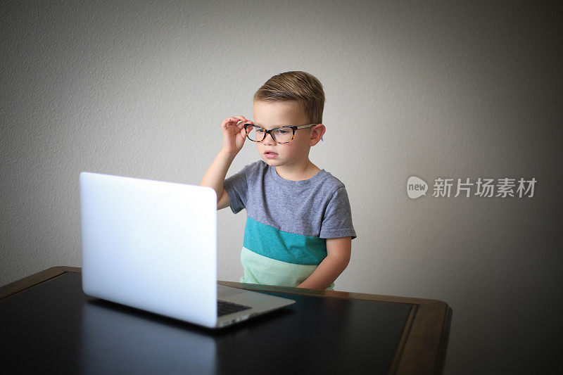 戴着眼镜的小男孩在用笔记本电脑