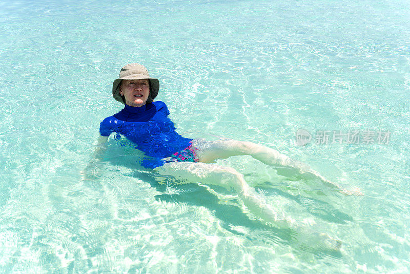年长妇女享受躺在浅水在小岛屿海滩四月，马尔代夫