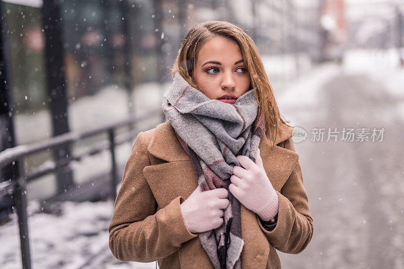 一个年轻女子在一个下雪的冬日在城市里取暖。