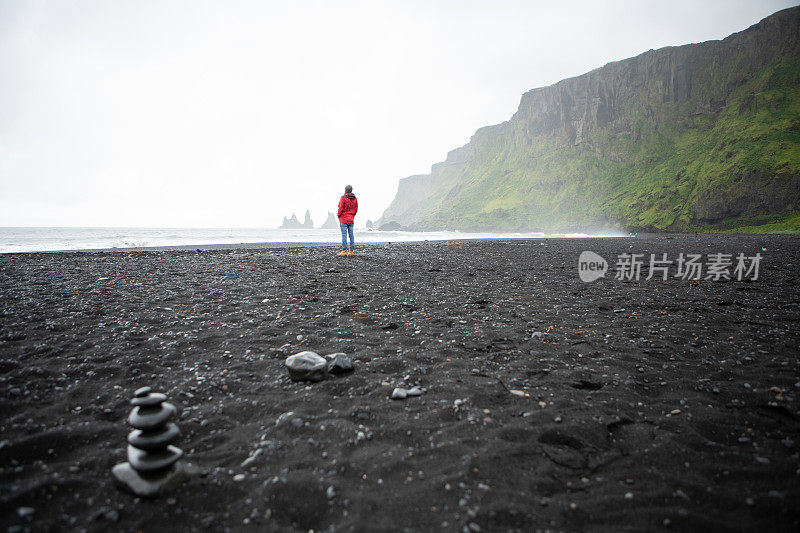 一个年轻人站在冰岛的黑沙滩上凝视着大海