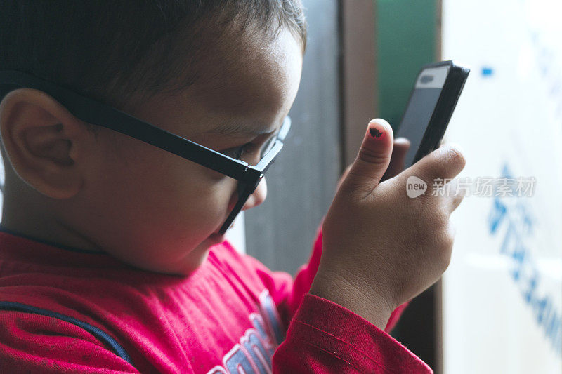 可爱的小男孩使用智能手机和戴眼镜