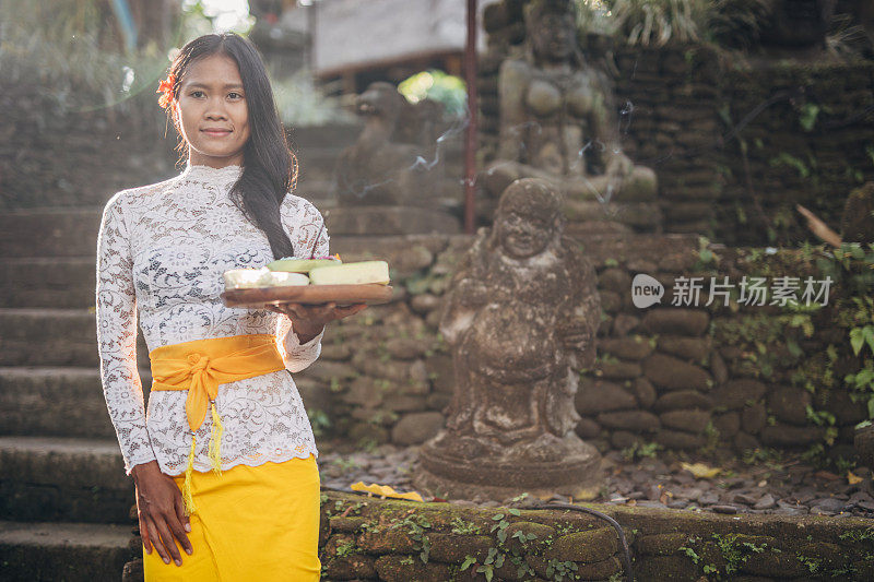 亚洲妇女，穿着传统服装，手持盛有鲜花的盘子