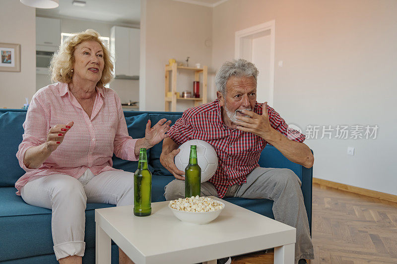一对幸福的白发夫妇在电视上看足球比赛。