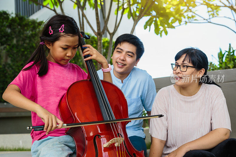 亚洲女孩与她的家人在户外公园演奏大提琴，听音乐的概念
