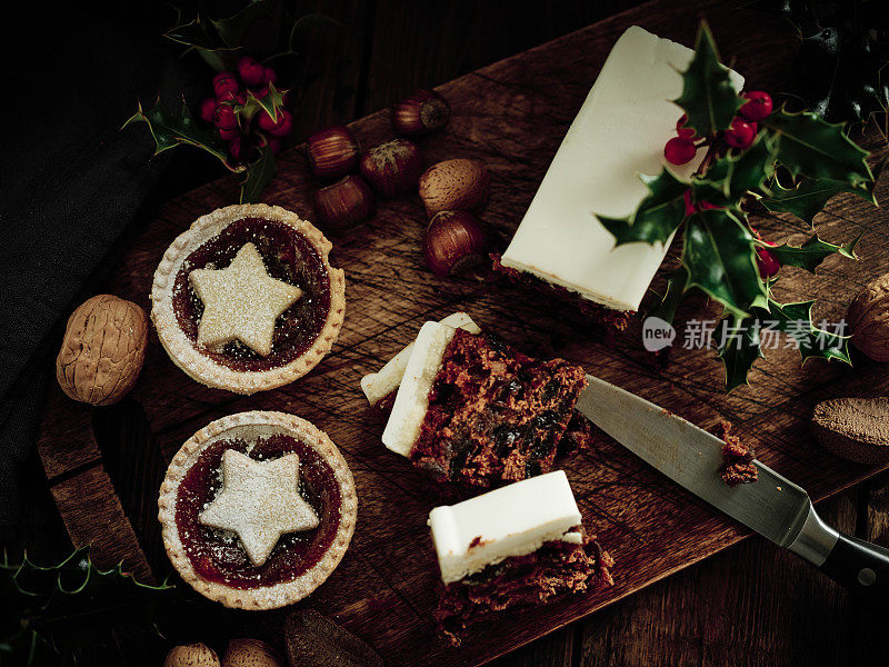 圣诞食品，肉馅饼，圣诞蛋糕，混合坚果和冬青在一个老化的深色木头表面。