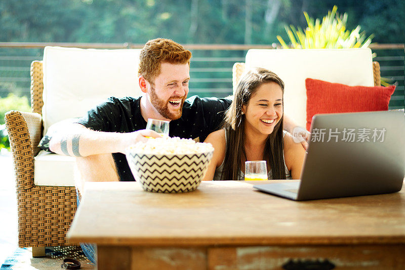 年轻夫妇在笔记本电脑上看电影，在客厅吃爆米花