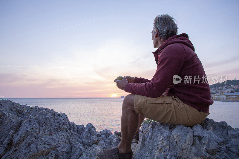 日出时，一个成熟的男人坐在海上的岩石脊上