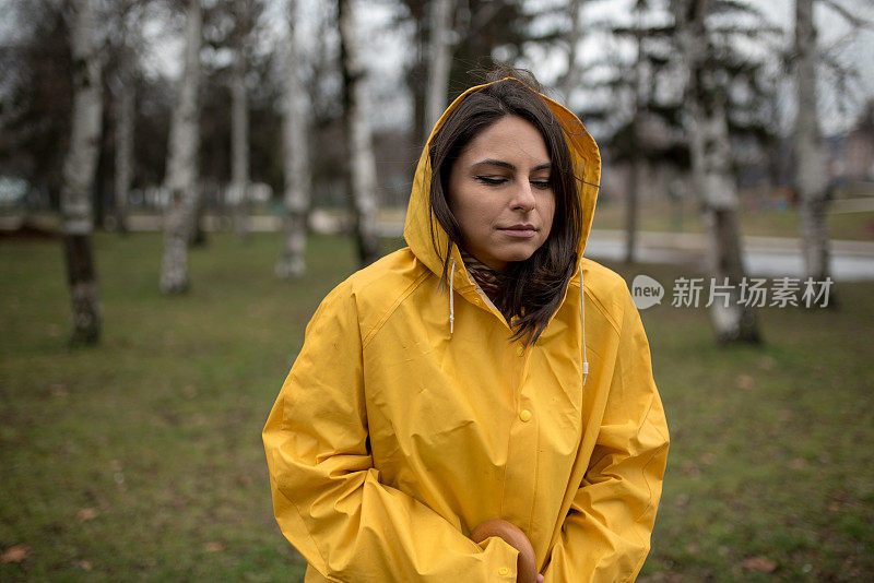 穿着黄色雨衣的年轻女子在公园里度过雨天