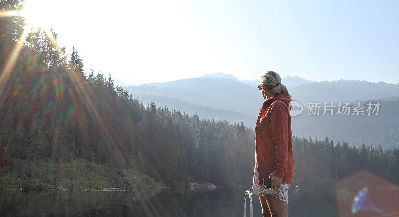 一个成熟的女人停在木码头上，眺望着湖面