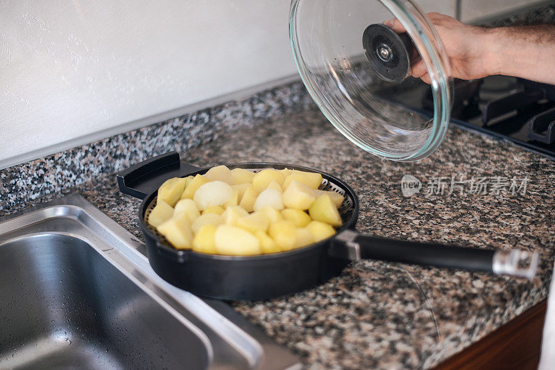 隔离烹饪:一个人从煮熟的土豆的锅上取下盖子