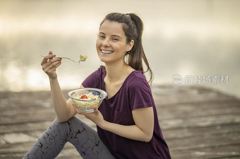 运动女性吃素食沙拉，坐在湖边码头上