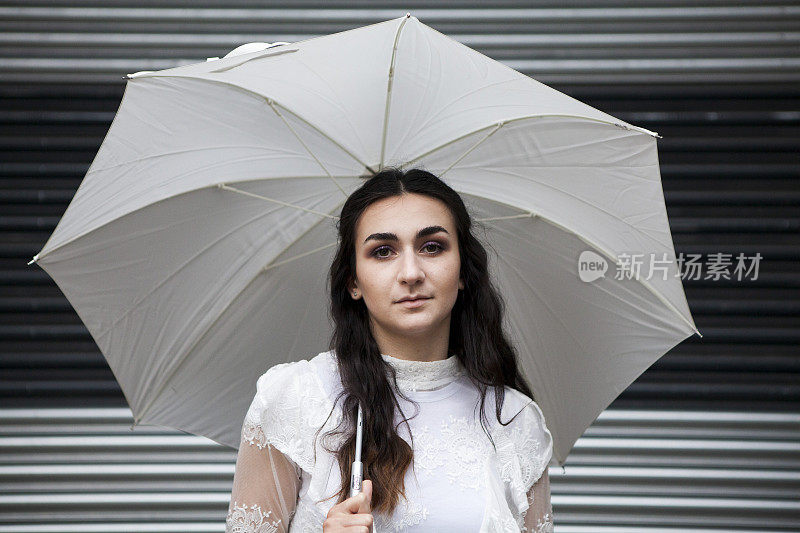 时尚的肖像年轻女子拿着一把白色的伞站在金属百叶窗前