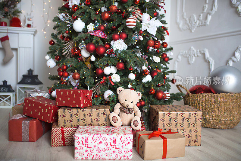在白色的客厅里，一棵红色和白色装饰的圣诞树下，礼物在盒子里特写。新的一年,