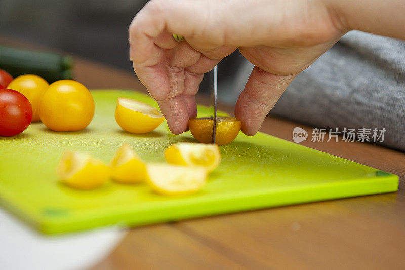 用手在绿色砧板上切一个黄色的樱桃番茄