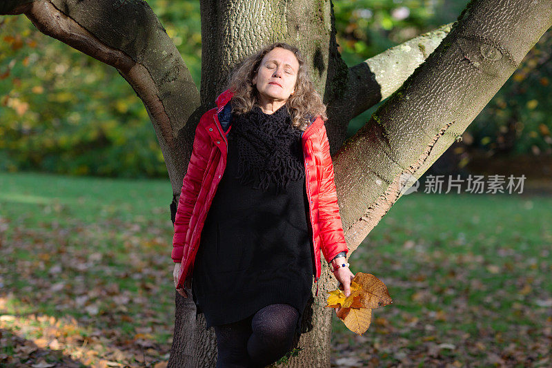 成熟的女人在秋天的户外，倚着树，闭着眼睛