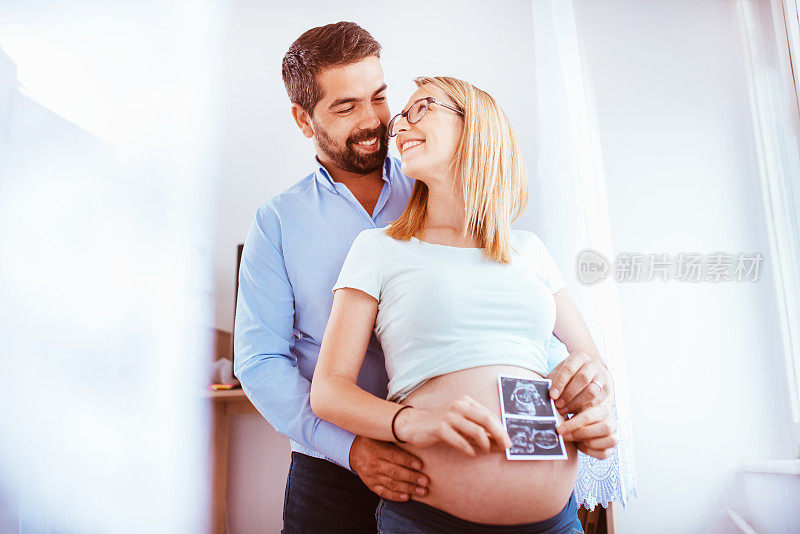 怀孕夫妇夫妇在家里感受到爱和放松。他们拿着超声波图像