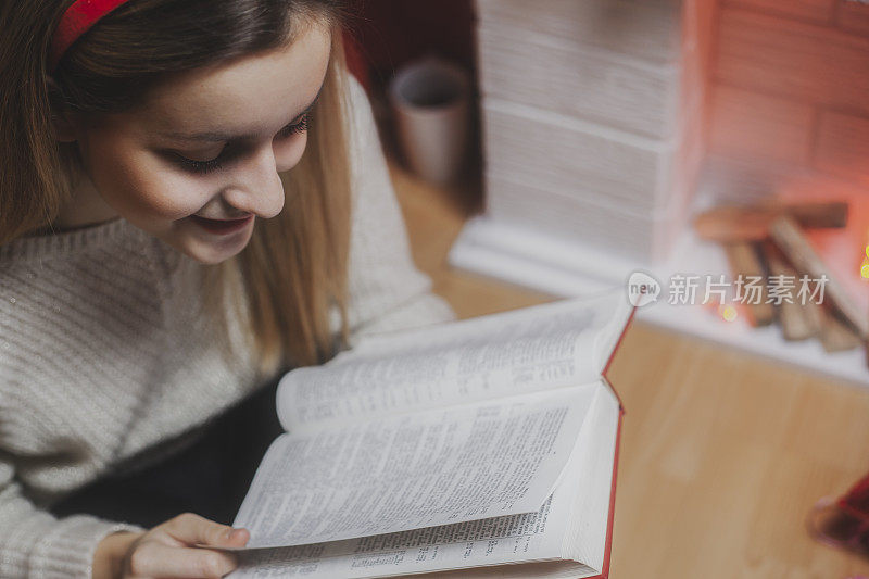 年轻女子在圣诞树下看书，在壁炉旁暖腿