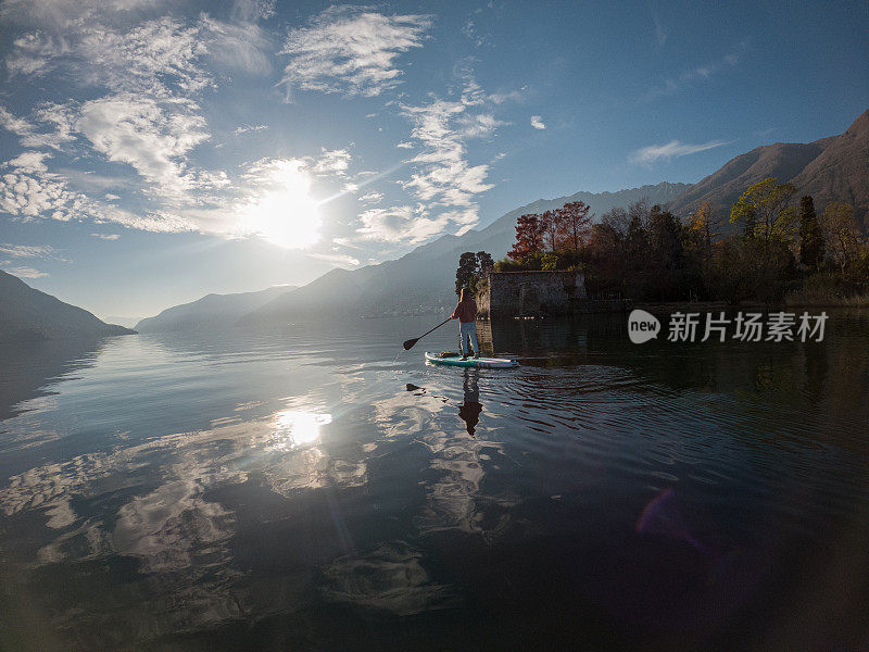 日落时分，女人在湖上站立式划桨板上划水